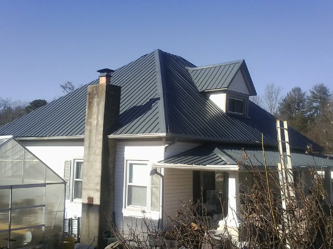 Dark blue standing seam metal roof on a white farmhouse with dormer — Slate & Tile Roof Repair by Roofing Brothers in Logan
