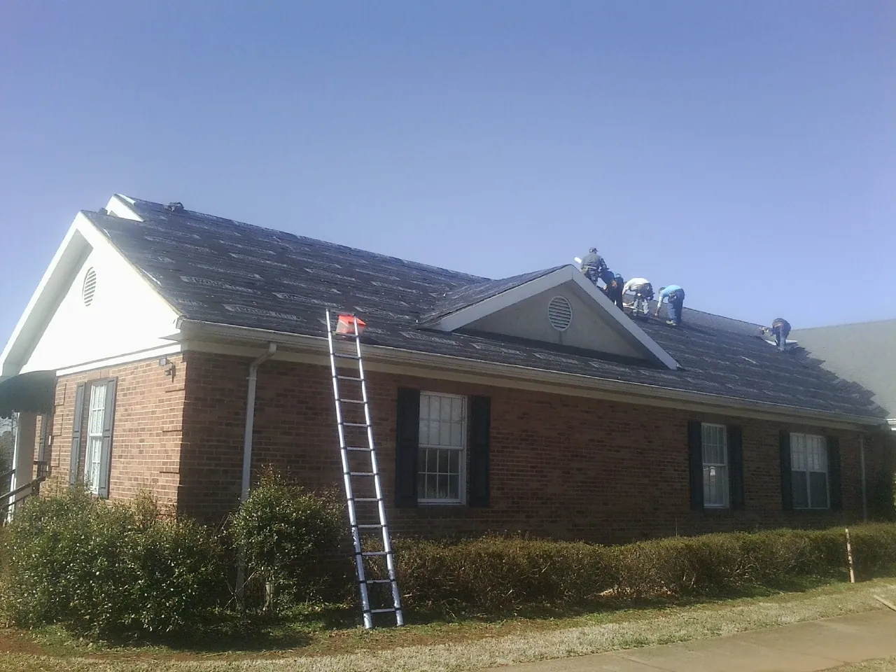 Crew tearing shingles off a brick ranch roof with a ladder set — Metal Roof Repair work by our crew in Logan