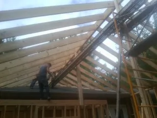 Rafters going up over a new addition with a worker on the wall in Logan