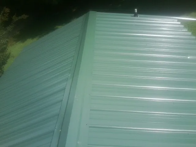 New green metal panels meeting at the ridge of a roof — Flat Roof Repair work by our crew in Logan